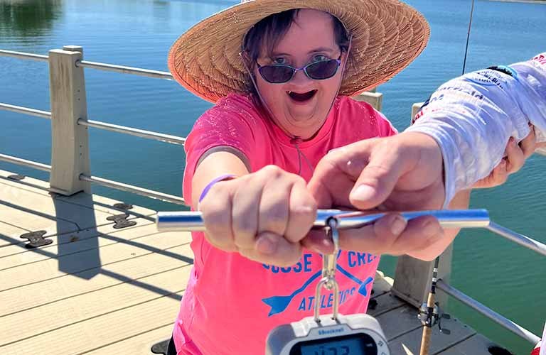 female fishing Woman smiling wearing a hat and sunglasses and holding up a fishing scale.